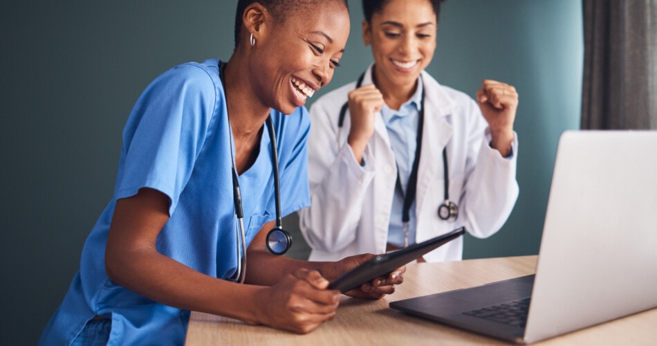two female healthcare practitioners happily reading on a tablet